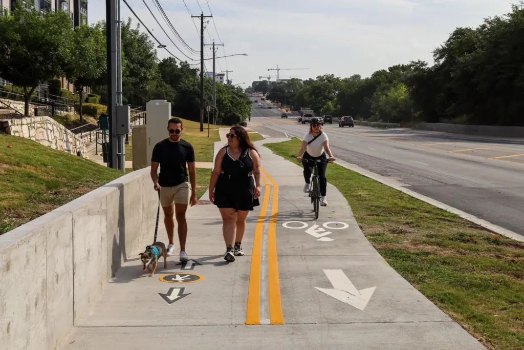 Shared use path on Congress & Ramble, featuring a cyclist, as well as pedestrians walking a dog 